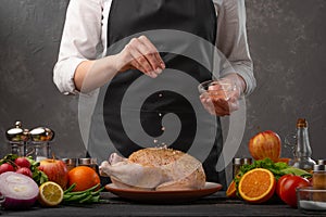 Cooking chicken by the chef sprinkling with coarse sea salt on a background of vegetables. Cookbook, and recipe book