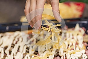 Cooking concept - cook hand adding grated cheese to pizza at pizzeria. Chef`s hand pouring spices on pizza