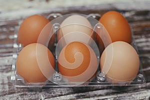 Set of six fresh brown eggs on clear plastic box. Wooden table background.