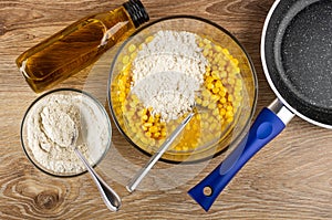 Cooking corn pancakes. Bottle of vegetable oil, bowl with flour, fork in bowl with mix of eggs, flour and corn, frying pan on