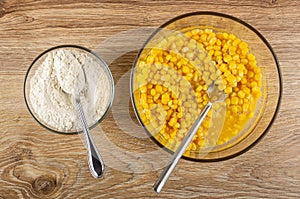 Cooking corn pancakes. Spoon in bowl with flour, fork in bowl with mix of eggs and corn on table. Top view