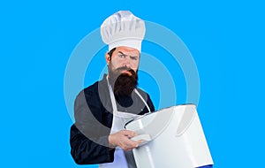 Cooking, culinary, food preparation. Serious bearded man in chef hat and uniform with casserole or saucepan. Cookware