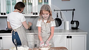 cooking with daughter, adorable female child preparing pastry dough and clapping hands with flour on background of mom