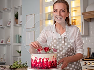 Cooking and decoration of cake with cream. Young woman pastry chef in the kitchen decorating red velvet cake