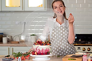 Cooking and decoration of cake with cream. Young woman pastry chef in the kitchen decorating red velvet cake.