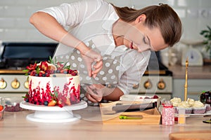 Cooking and decoration of cake with cream. Young woman pastry chef in the kitchen decorating red velvet cake