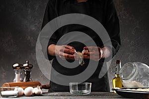 Cooking dough. Chef breaks an egg to anoint buns. Bakery, baker prepares fresh buns, bread on a background of ingredients