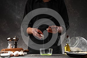 Cooking dough. Chef breaks an egg to anoint buns. Bakery, baker prepares fresh buns, bread on a background of ingredients