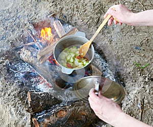 Cooking on fire at picnic, food prepared in pot on wood, potatoes and tomatoes, healthy vegetarian food, woman hands with spoon