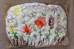 Cooking Focaccia. Raw focaccia creatively decorated with vegetables on parchment paper. Sourdough dough