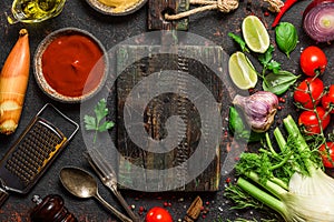 Cooking food background. Frame of spices, herbs and fresh vegetables with cutting board and utensils on black table