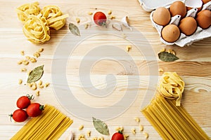 Cooking food background with free space for text. Composition with pasta, tomato, eggs, garlic, bay leaf over the wood background