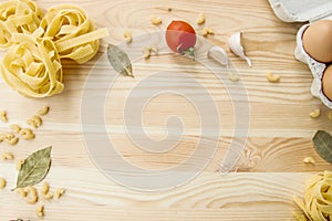 Cooking food background with free space for text. Composition with pasta, tomato, eggs, garlic, bay leaf over the wood background