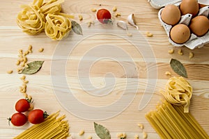 Cooking food background with free space for text. Composition with pasta, tomato, eggs, garlic, bay leaf over the wood background