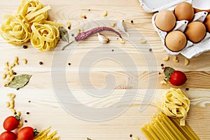 Cooking food background with free space for text. Composition with pasta, tomato, eggs, garlic, bay leaf over the wood background