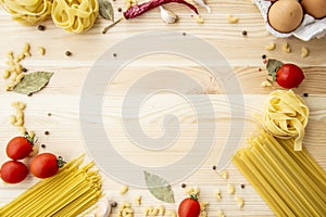 Cooking food background with free space for text. Composition with pasta, tomato, eggs, garlic, bay leaf over the wood background
