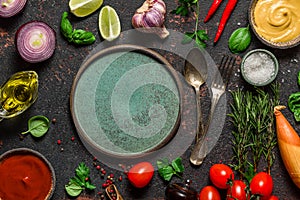 Cooking food background. Plate with cutlery in frame made of fresh vegetables, spices, herbs and sauces. Top view