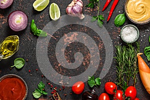Cooking food composition. Frame made of fresh vegetables, spices, herbs and sauces on black stone background. Top view