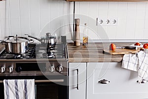 Cooking food on modern kitchen with steel oven, pots, knife on wooden cutting board with vegetables, pepper, spices,oil on wooden