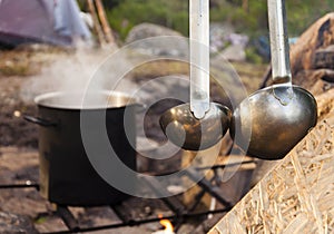 Cooking food in the nature. Big pot on fire and ladle in forest.