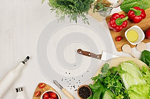 Cooking fresh raw spring salad of green and red vegetables, spices, oil with wooden kitchenware on white wooden background, border