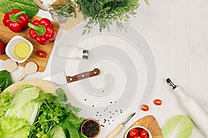 Cooking fresh raw spring salad of green and red vegetables, spices, oil with wooden kitchenware on white wooden background, border