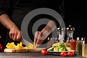 Cooking fresh salad, the chef cuts the paprika on the background of vegetables. Vegetables and healthy eating