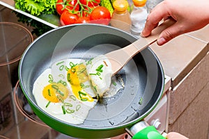 Cooking fried scrambled eggs, hands with a wooden spatula