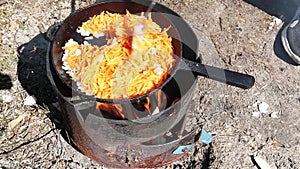 Cooking frying with carrots and onions in a pan in the field