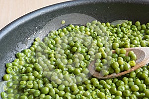 Cooking green peas in black frying pan with wooden spoon