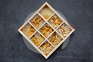 Cooking, healthy food concept. Different types of pasta in a wooden box on a dark background. View from above