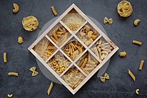 Cooking, healthy food concept. Different types of pasta in a wooden box on a dark background. View from above