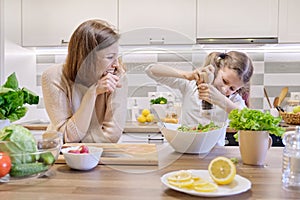 Cooking healthy home meal by family. Girl salts freshly cooked salad, mother looks up and rejoices