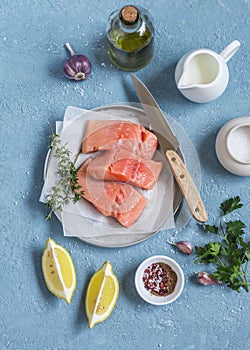 Cooking healthy lunch - raw salmon, lemon, olive oil, spices and herbs on a blue background.