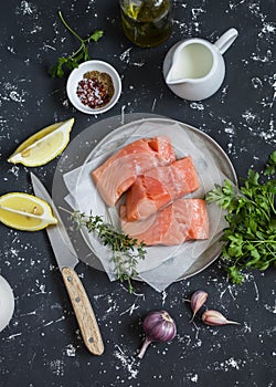 Cooking healthy lunch - raw salmon, lemon, olive oil, spices and herbs on a dark background.