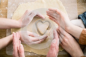 Cooking and home concept - close up of female hands making cookies from fresh dough at home. Hands of three women hold