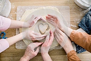 Cooking and home concept - close up of female hands making cookies from fresh dough at home. Hands of three women hold