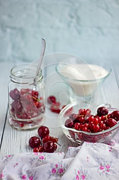 Red berries in a glass transparent bowl and sugar; currants in a jar on a light background