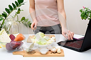 Cooking at home a woman watches online video recipes on a laptop and cooks in the kitchen at home Pickled pink cabbage
