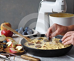 Cooking homemade apple and plum pie. Elderly woman is hands put plum pieces on charlotte dough in a frying pan. Woman is hobby.