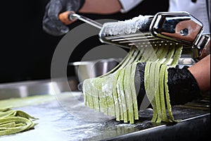 Cooking homemade pasta with spinach. Machine for making pasta. Unrecognizable person. Side view. Close up. Photo on a black