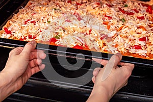 Cooking homemade pizza in the oven. A young woman puts uncooked pizza in the oven on a baking pan. Appetizing pizza with delicious