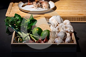 Cooking ingredient, lime, mushroom, shallot, lemon grass, spring onion, chilli, bergamot leaves and cheese in wood box plate. They