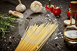 Tomatoes garlic salt olive peppers and pasta on a black table