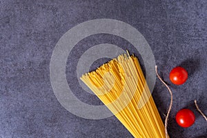 Bunch of raw Italian pasta with cherry tomatoes isolated on stone grey background.