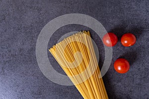 Bunch of raw Italian pasta with cherry tomatoes isolated on stone grey background.