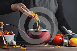 Cooking italian pasta in a pot in the kitchen, Chef preparing food, meal. The woman-the cook throws into the pot the pasta fusilli