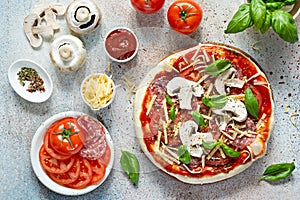 Cooking Italian pizza with tomato sauce, fresh tomatoes, cheese, mushrooms, salami slices  and basil .
