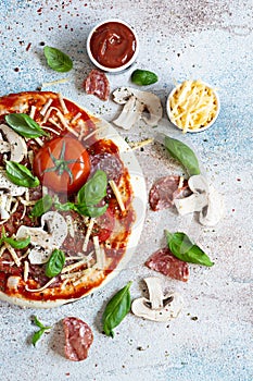 Cooking Italian pizza with tomato sauce, fresh tomatoes, cheese, mushrooms, salami slices and basil .