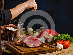 Cooking juicy steaks from beef, pork by a professional chef on a dark blue background. Raw meat, vegetables, spices on a wooden
